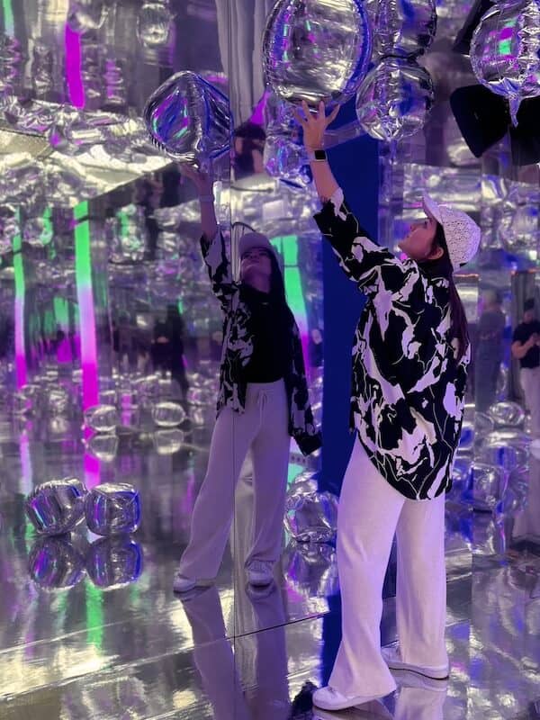 Frau in einem Spiegelraum, mit silbernen Luftballons.